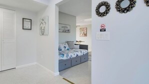 A bedroom with a bed, a nightstand, a wall-mounted mirror, and a door with a louvered window. - 3/2 Heated Pool • Close to Beach • Trails • Golf (Port St. Lucie)