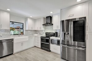 A modern kitchen with white cabinetry, stainless steel appliances, and a window with a view. - Modern Coastal Family Friendly Home Minutes to Las Olas & Fort Lauderdale Beach (Fort Lauderdale)