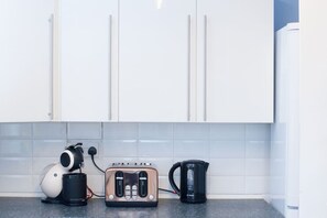 A kitchen with white cabinets, a toaster, a coffee maker, and a kettle on the counter. - Chippings - Village life in the city. MyCityHaven (Stapleton)