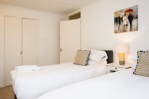A hotel room with two beds, a nightstand with a lamp, and a painting on the wall. - Chippings - Village life in the city. MyCityHaven (Stapleton)