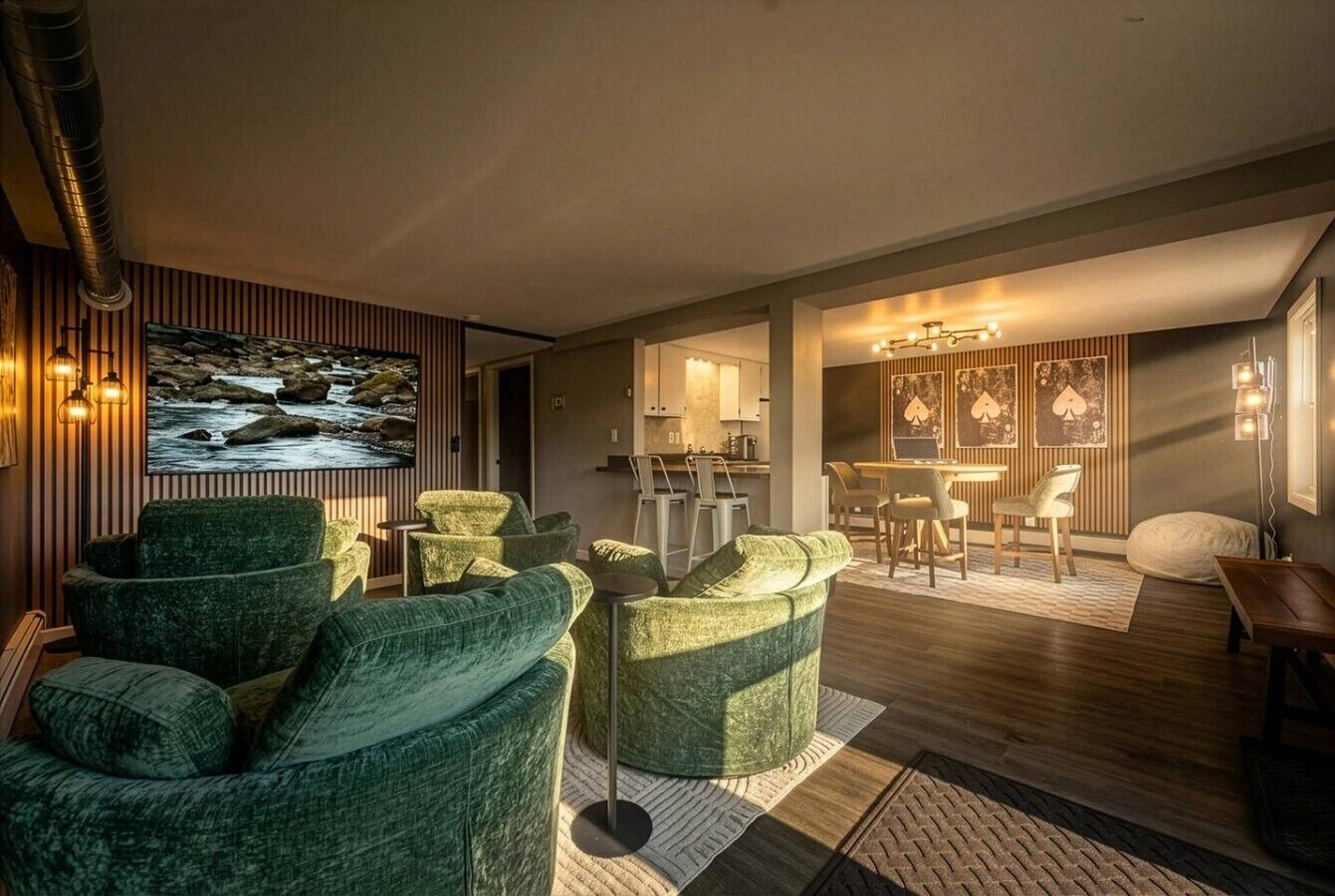 A modern living room with green upholstered sofas, a flat-screen TV, and a dining area with a wooden table and chairs.