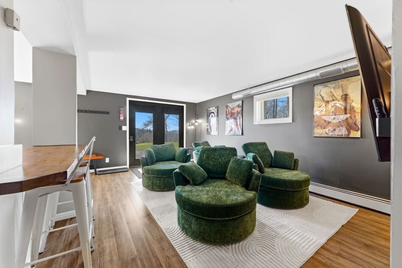 A modern interior with a wooden dining table, green upholstered chairs, a white ladder, and a large window with a view.