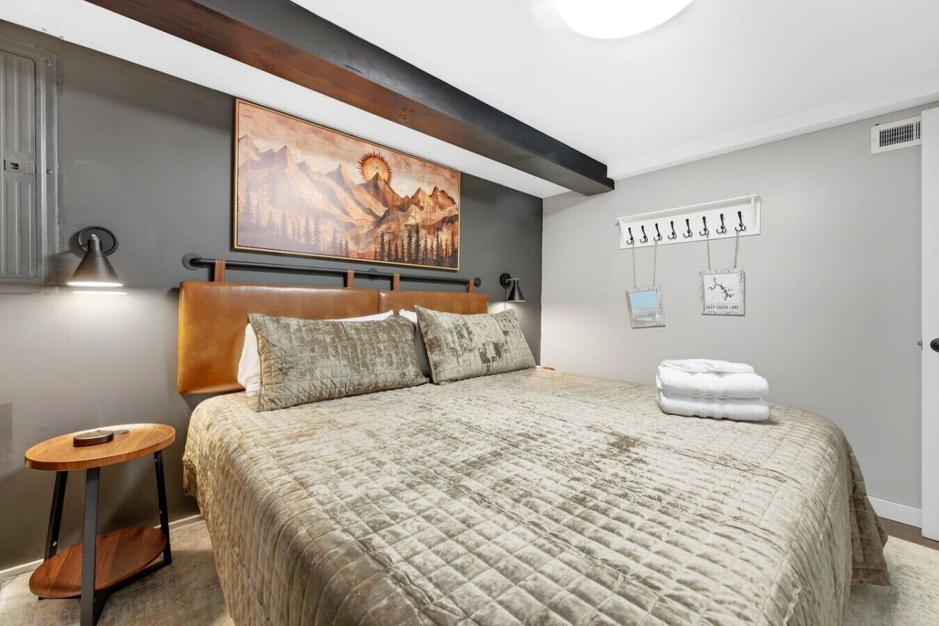 Un dormitorio con una cama grande, un cabecero, un cuadro sobre la cama, una mesita de noche y un perchero con ganchos.