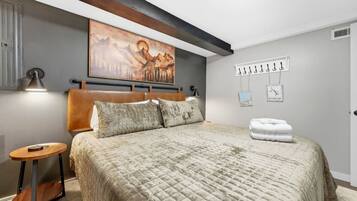 Un dormitorio con una cama grande, un cabecero, un cuadro sobre la cama, una mesita de noche y un perchero con ganchos.