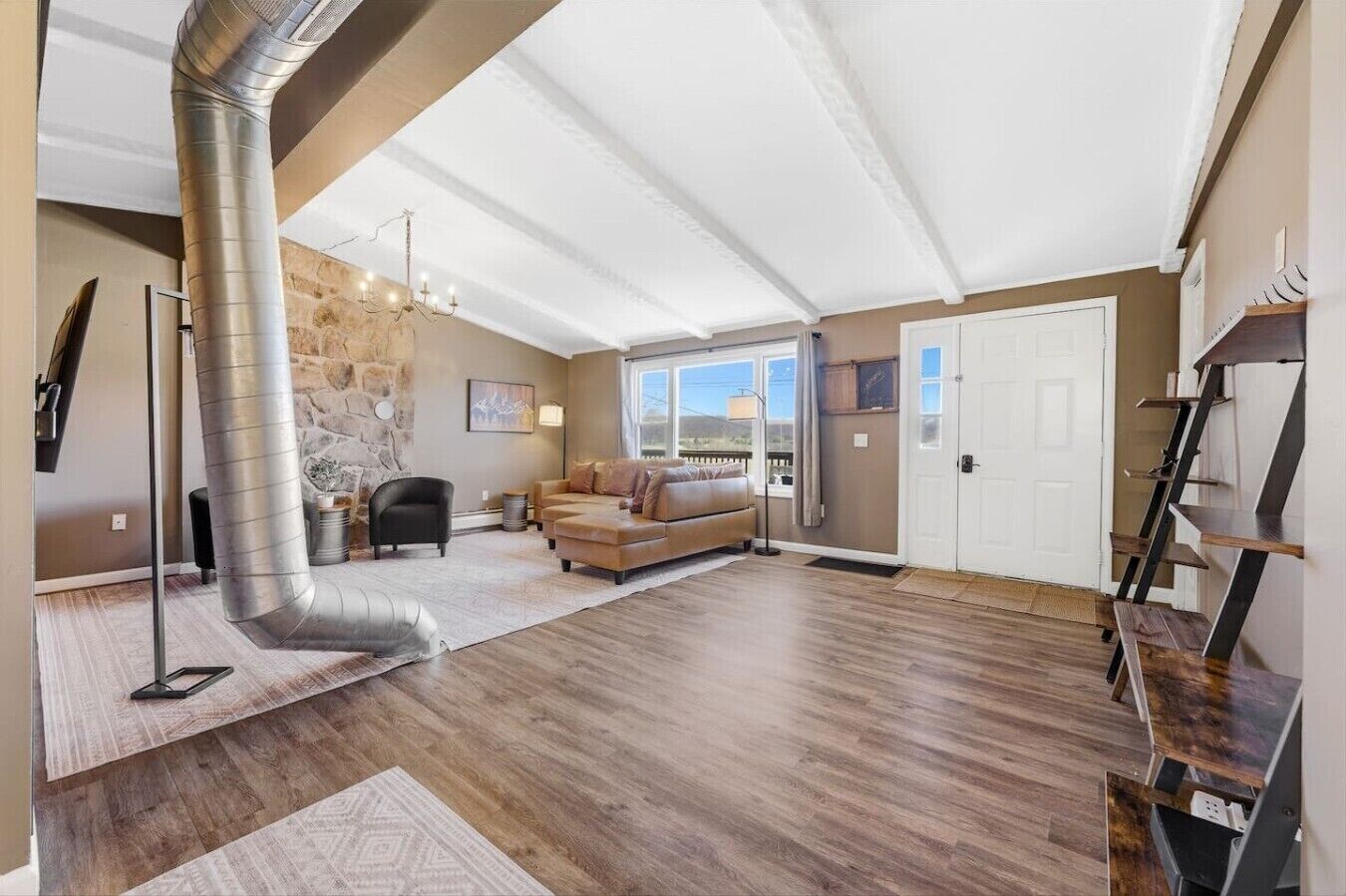 A spacious living room with a stone wall, a fireplace, a sofa, and a staircase.