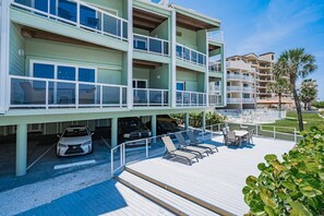 A multi-story hotel with balconies, a covered parking area, and a poolside lounge. - 2BR | Coastal Condo Steps to Beach, Fully Equipped (Indian Shores)