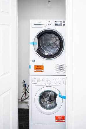 A stacked washer and dryer unit with control panels and maintenance stickers. - Garden View by MyCityHaven (Redland)