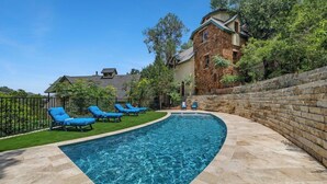 Una piscina con sillas reclinables azules, un edificio de piedra y un muro de ladrillo.