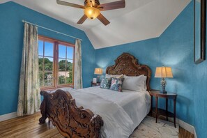 Ein Schlafzimmer mit einem großen Bett, einem Deckenventilator, zwei Nachttischlampen und einem Fenster mit Vorhängen.