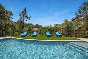 A swimming pool with four blue lounge chairs and a black fence. - Lucy In The Sky (Austin)