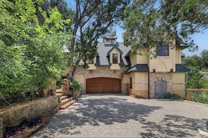 A two-story house with a stone facade, a wooden garage door, and a paved driveway. - Lucy In The Sky (Austin)