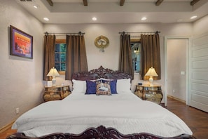 A large bed with ornate headboard, two bedside tables with lamps, and a decorative wall piece. - Lucy In The Sky (Austin)