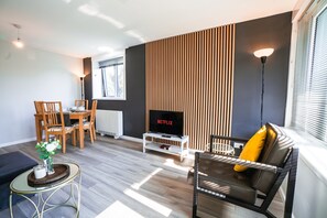 A modern living room with a TV, wooden panel wall, and a sofa with a yellow pillow. - Spacious Oxford Apartment | Near JR Hospital & (Headington)