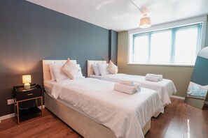 A bedroom with two beds, a nightstand with a lamp, a window with blinds, and a mirror. - Spacious Oxford Apartment | Near JR Hospital & (Headington)