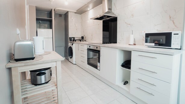 Une cuisine moderne équipée d’un lave-linge, d’un four, d’un four à micro-ondes et d’une machine à café, le tout intégré.