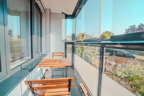 A balcony with a wooden bench and a table, overlooking a street with cars and trees. - Spacious Oxford Apartment | Near JR Hospital & (Headington)