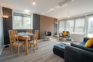 A modern living room with a dining area, a sofa, and a TV. - Spacious Oxford Apartment | Near JR Hospital & (Headington)