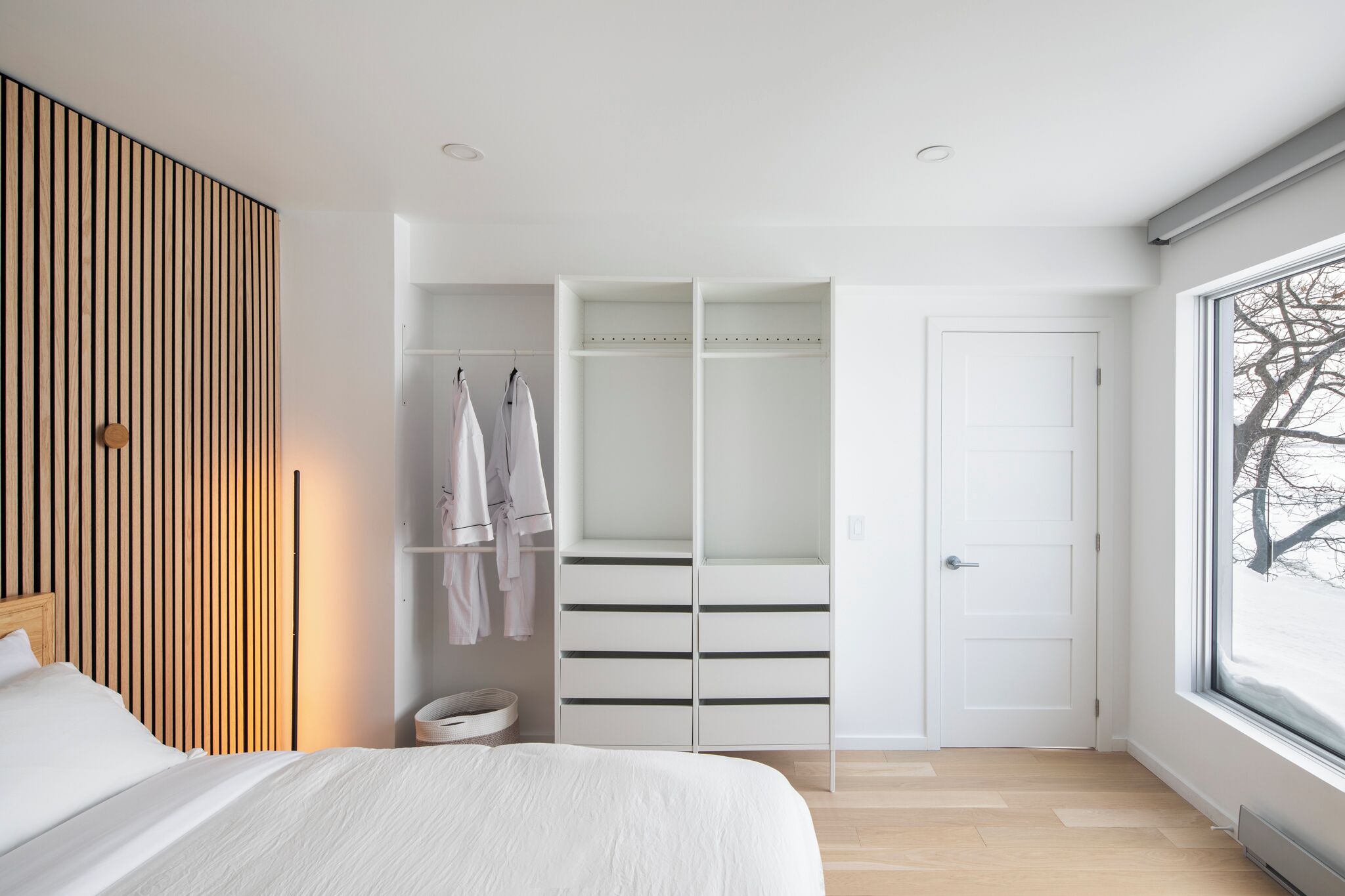 Une chambre à coucher comprenant un lit, une armoire avec espace pour suspendre les vêtements et une fenêtre donnant sur des arbres.