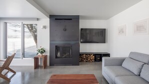 Una sala de estar moderna con chimenea, un sofá, un televisor montado en la pared y un ventanal grande.