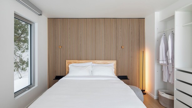 Un dormitorio moderno con una cama grande, un panel de pared de listones de madera, una ventana y un armario.