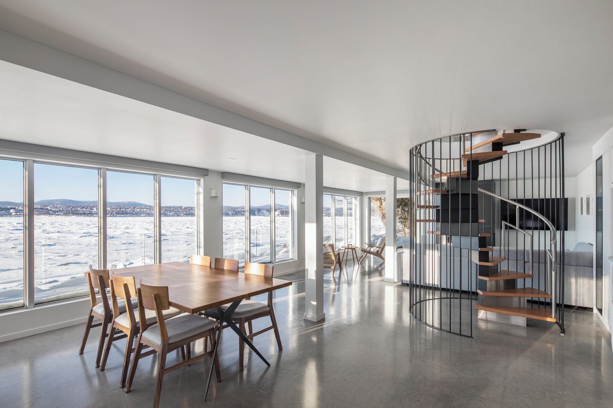 A spacious interior with a large dining table, a spiral staircase, and a view of a snowy landscape.