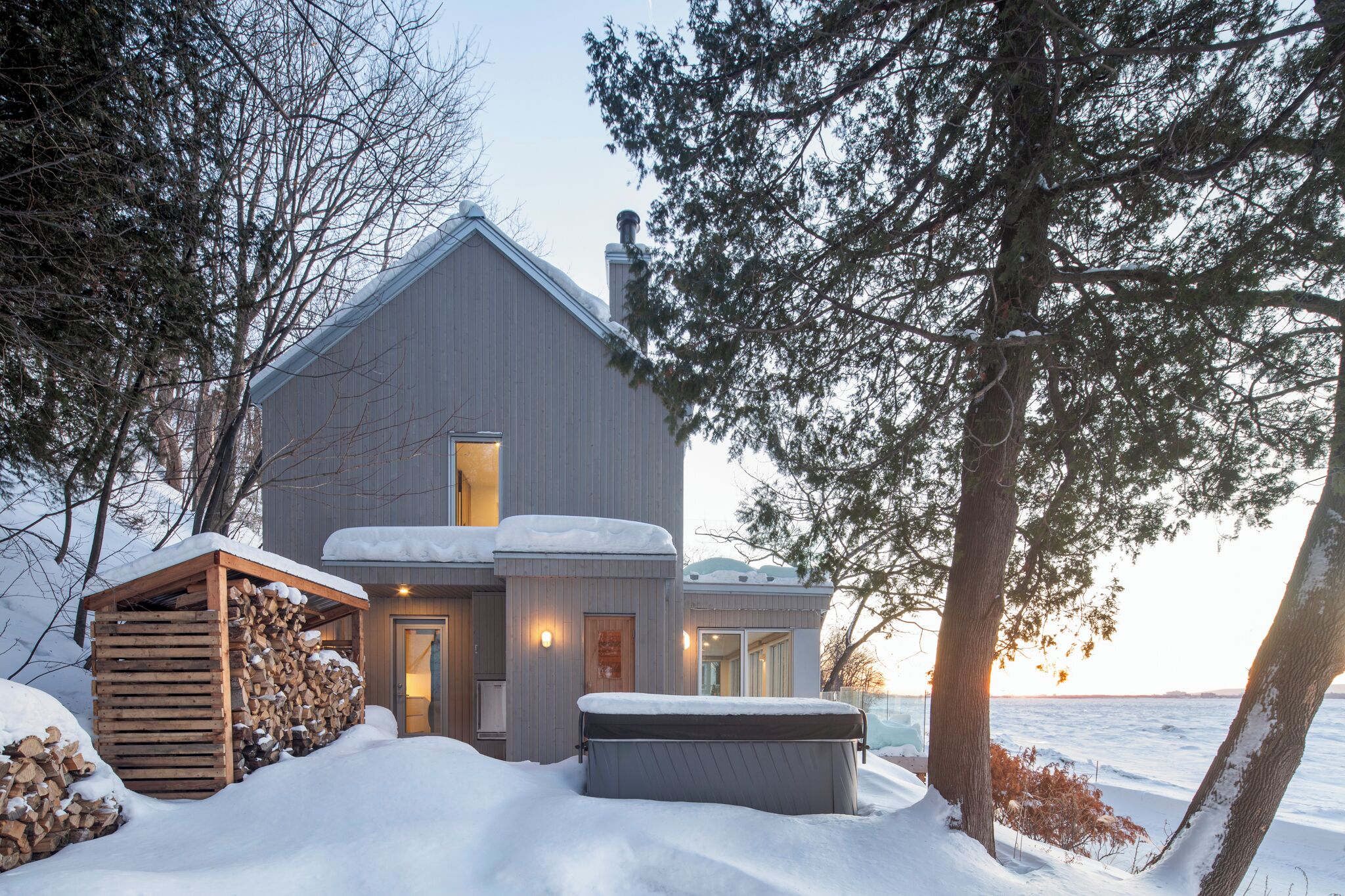 A cabin with a large deck, a hot tub, and a snow-covered landscape.