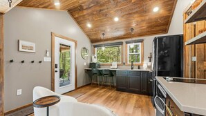 Cocina moderna con armarios oscuros, un refrigerador negro grande y un comedor con una silla blanca y una mesa redonda pequeña.
