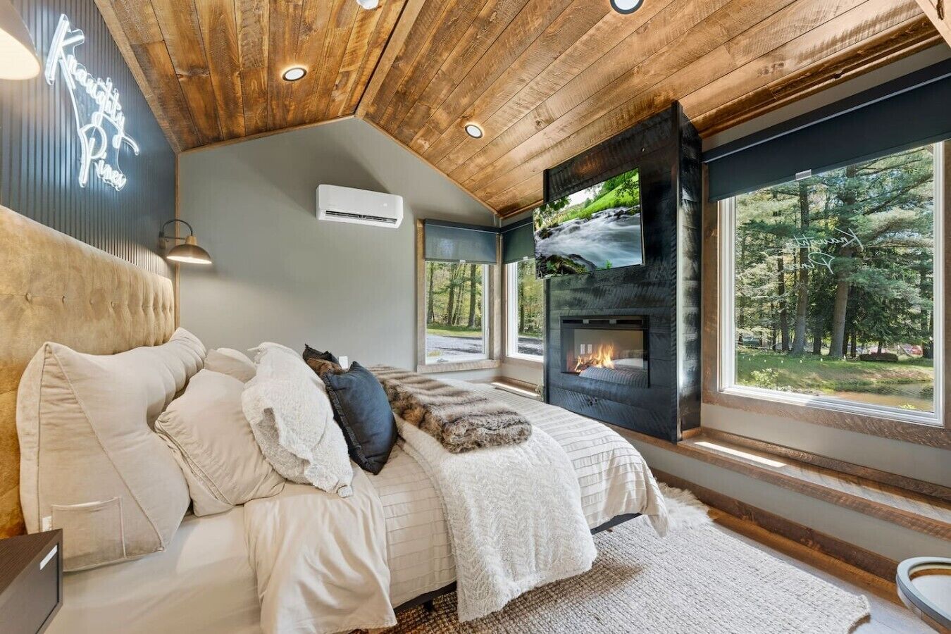 A bedroom with a bed, a fireplace, a TV, and a large window.