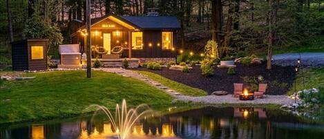 A cabin with a pond, outdoor seating, and a stone wall.