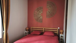 Un dormitorio con una cama, dos mesitas de noche, una lámpara de pared y una ventana con cortinas.