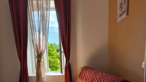 Una habitación con piso de madera, un sofá con una manta y una ventana con cortinas.