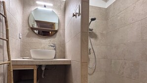 Un bagno con lavandino, specchio, doccia e una scala di legno.