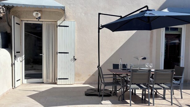 Un patio esterno con tavolo e sedie, un ombrellone grande e una porta con un numero.
