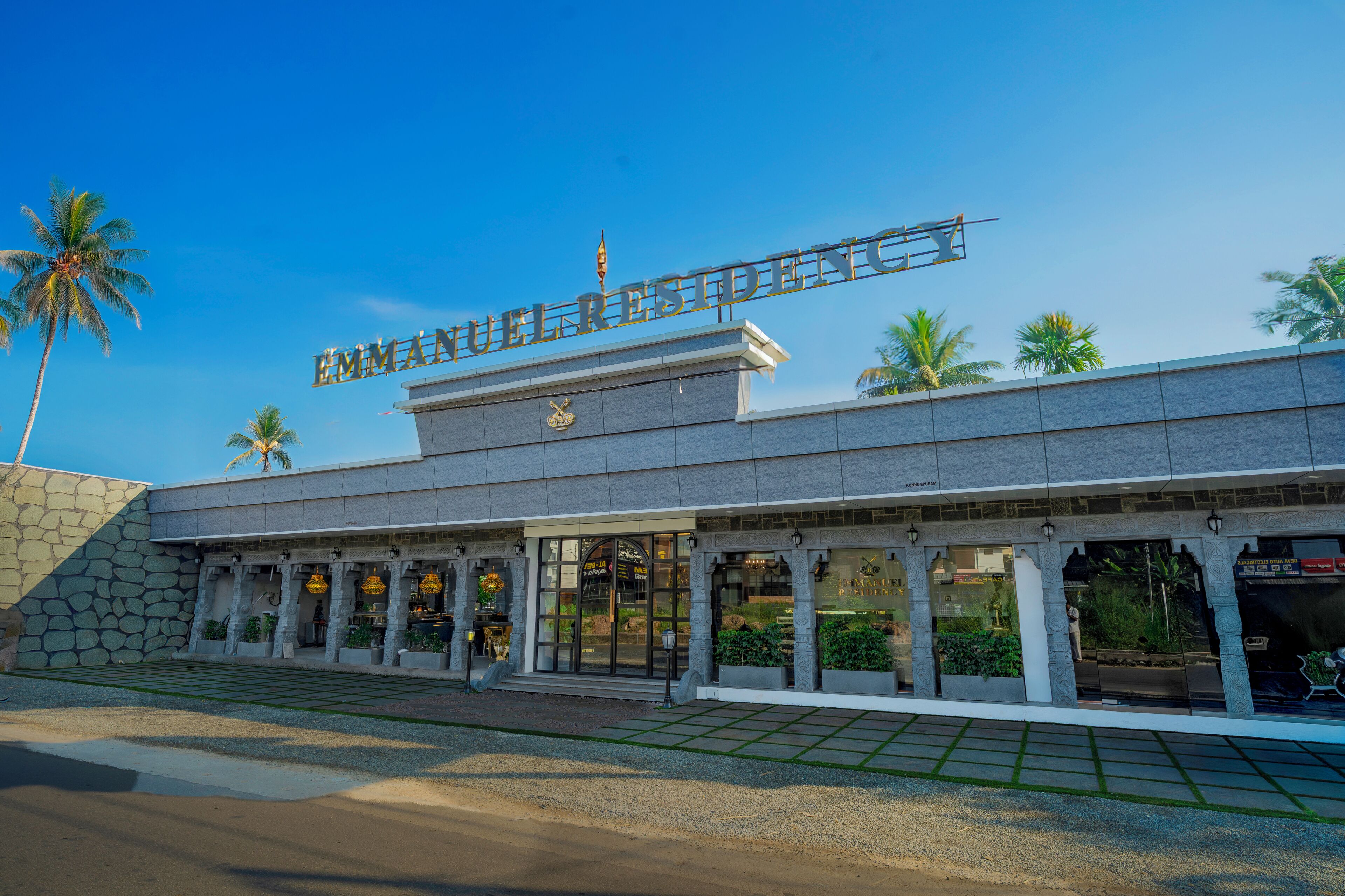A hotel entrance with a sign, palm trees, and a stone facade.