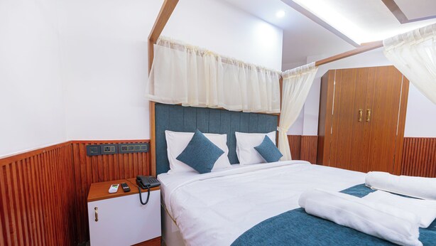 Habitación de hotel con cama, mesita de noche con teléfono y panel de control, armario y dosel.
