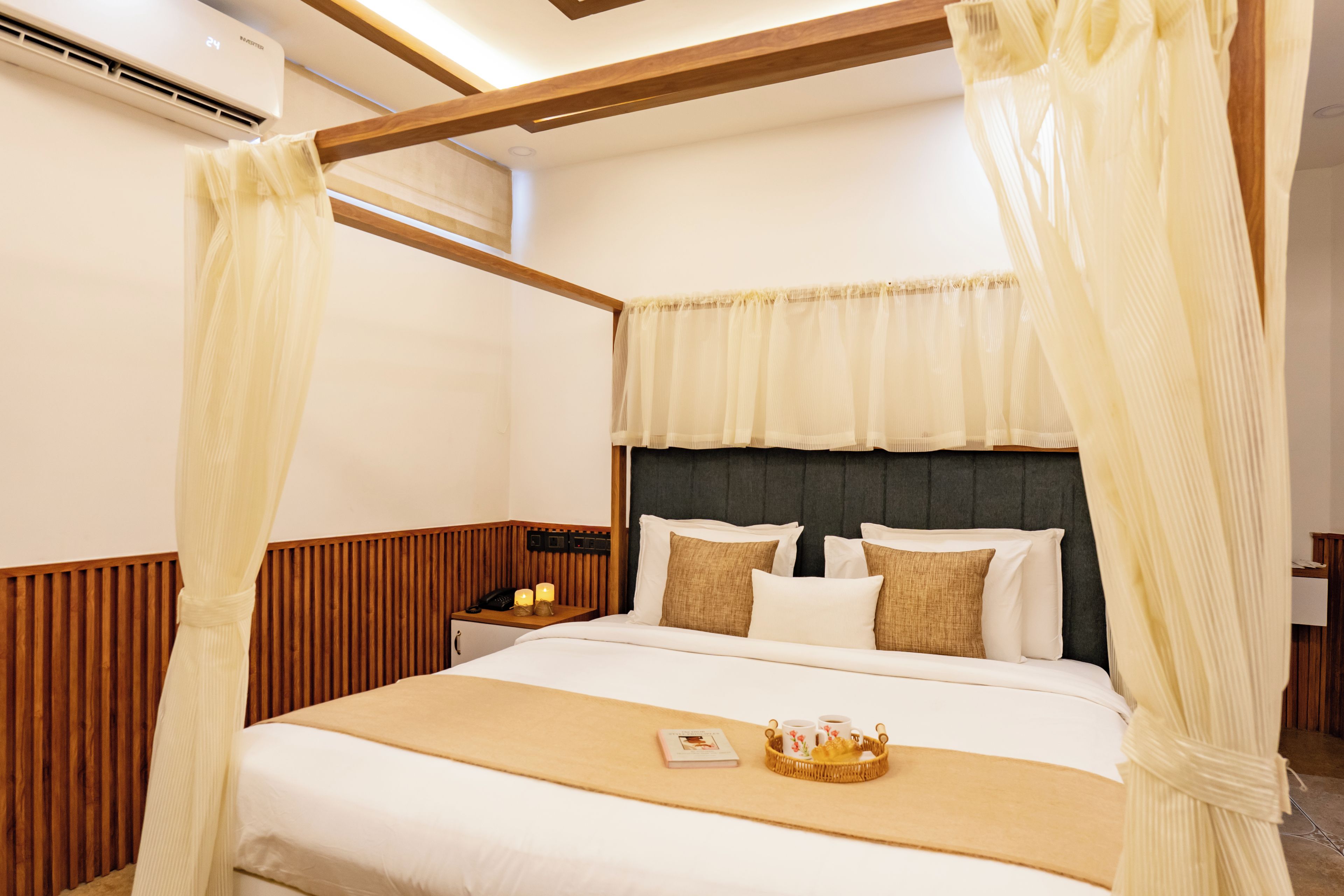 Habitación de hotel con cama con dosel, paneles de madera, mesita de noche con lámpara y mesita de noche con teléfono y velas.