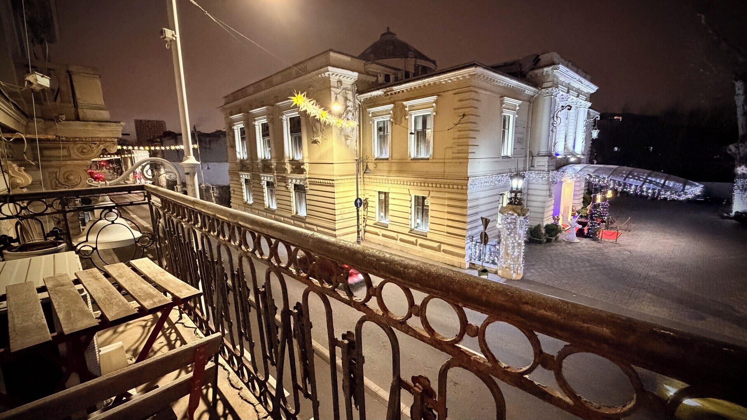 Un bâtiment historique à l’architecture classique, doté d’un balcon orné de rampes en métal ouvragé, et d’un sapin de Noël exposé à l’extérieur.