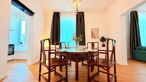 Een eethoek met een ronde tafel, vier houten stoelen, een vaas met bloemen en een kroonluchter.