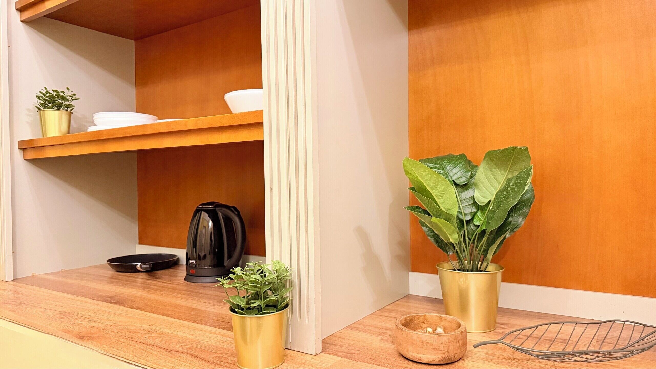 A kitchen area with a wooden countertop, a kettle, a small potted plant, and a larger potted plant.
