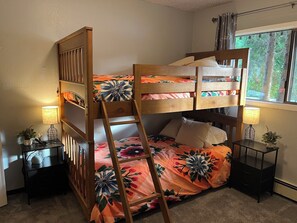 A bunk bed room with a ladder, two bedside tables with lamps, a window with curtains, and a floral bedspread. - Swan Lake Hacienda. A 2-bedroom apartment in Sitka, your home away from home. (Sitka)