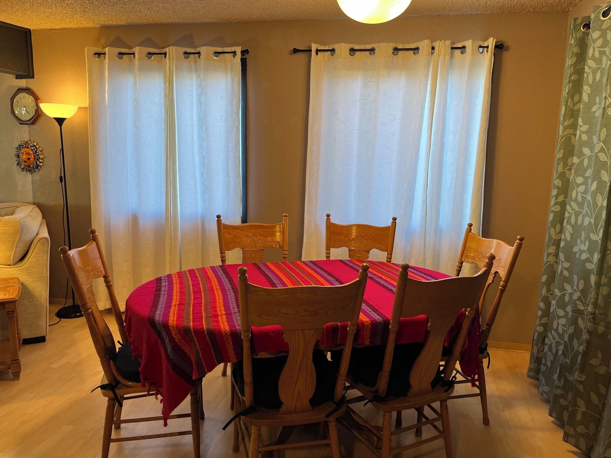 A dining area with a round table, six wooden chairs, and a red tablecloth.
