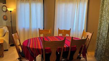 A dining area with a round table, six wooden chairs, and a red tablecloth.