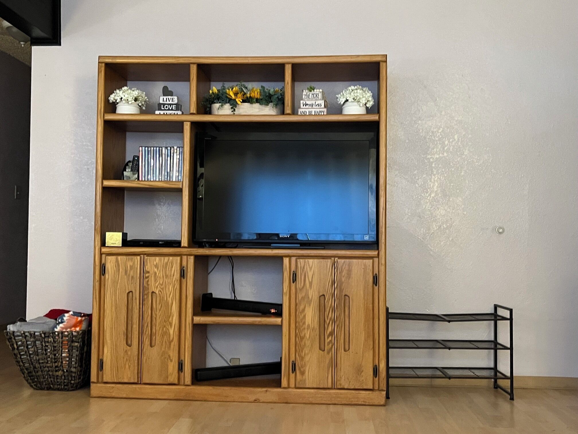 Een houten entertainmentkast met een flatscreentelevisie, planken met decoratieve objecten en een klein kastje.