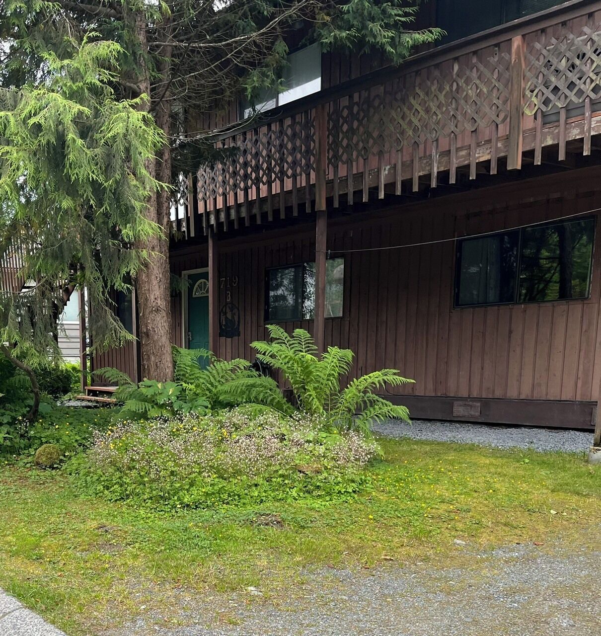 A wooden cabin with a porch, surrounded by lush greenery and a small pond.