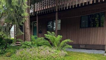 A wooden cabin with a porch, surrounded by lush greenery and a small pond.