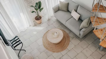 Ein Wohnzimmer mit grauem Sofa, einem runden gewebten Pouf, einer Zimmerpflanze und einem schwarzen Sessel.