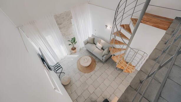 A modern living space with a sofa, a round table, a potted plant, and a spiral staircase. - Luminis Residence by All about Paxos (Gaios)