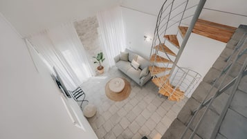 A modern living space with a sofa, a round table, a potted plant, and a spiral staircase.