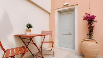 Un pequeño espacio al aire libre con una mesa y dos sillas, una planta en maceta, una puerta y una maceta grande.
