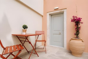 A small outdoor seating area with a table and two chairs, a potted plant, a door, and a large flower pot.